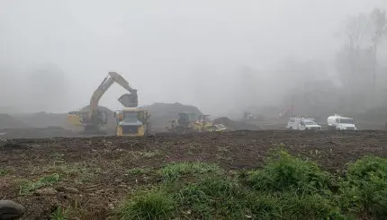 Foggy morning with construction equipment moving dirt in open field