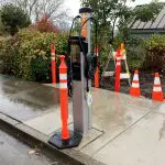 New electric vehicle charging station along road on a rainy day. Orange cone in front of station to block use.