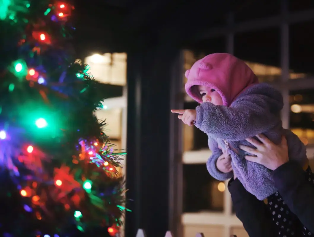 A young child looks at a lit up Christmas tree