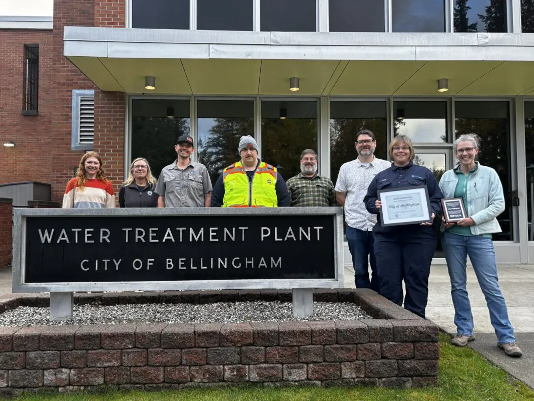 A group of people smile behind a "Water Treatment Plant" sign