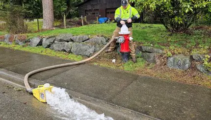man at hydrant as water rushes out hose down the street