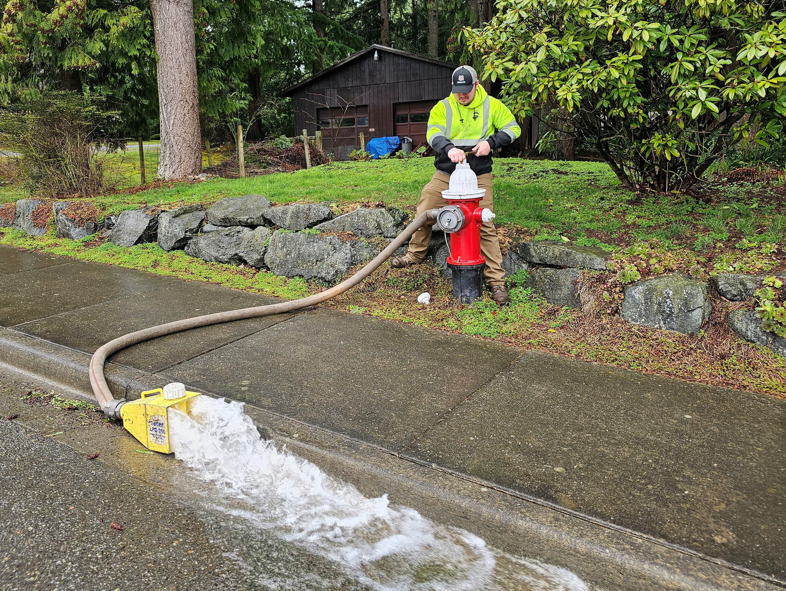 man at hydrant as water rushes out hose down the street