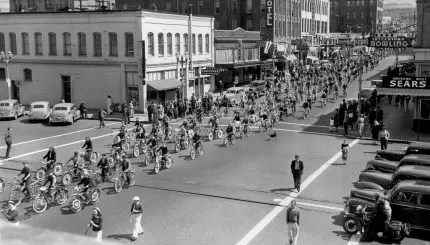 Historic photo of many youth on bicycles riding down street