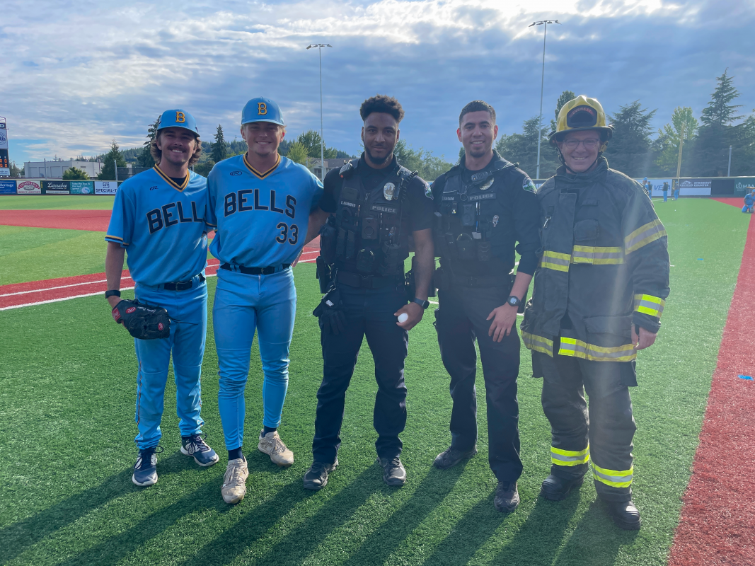 Two baseball players, two police officers, and a fire fighter smile together on a baseball field