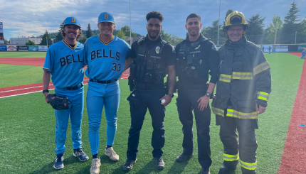 Two baseball players, two police officers, and a fire fighter smile together on a baseball field