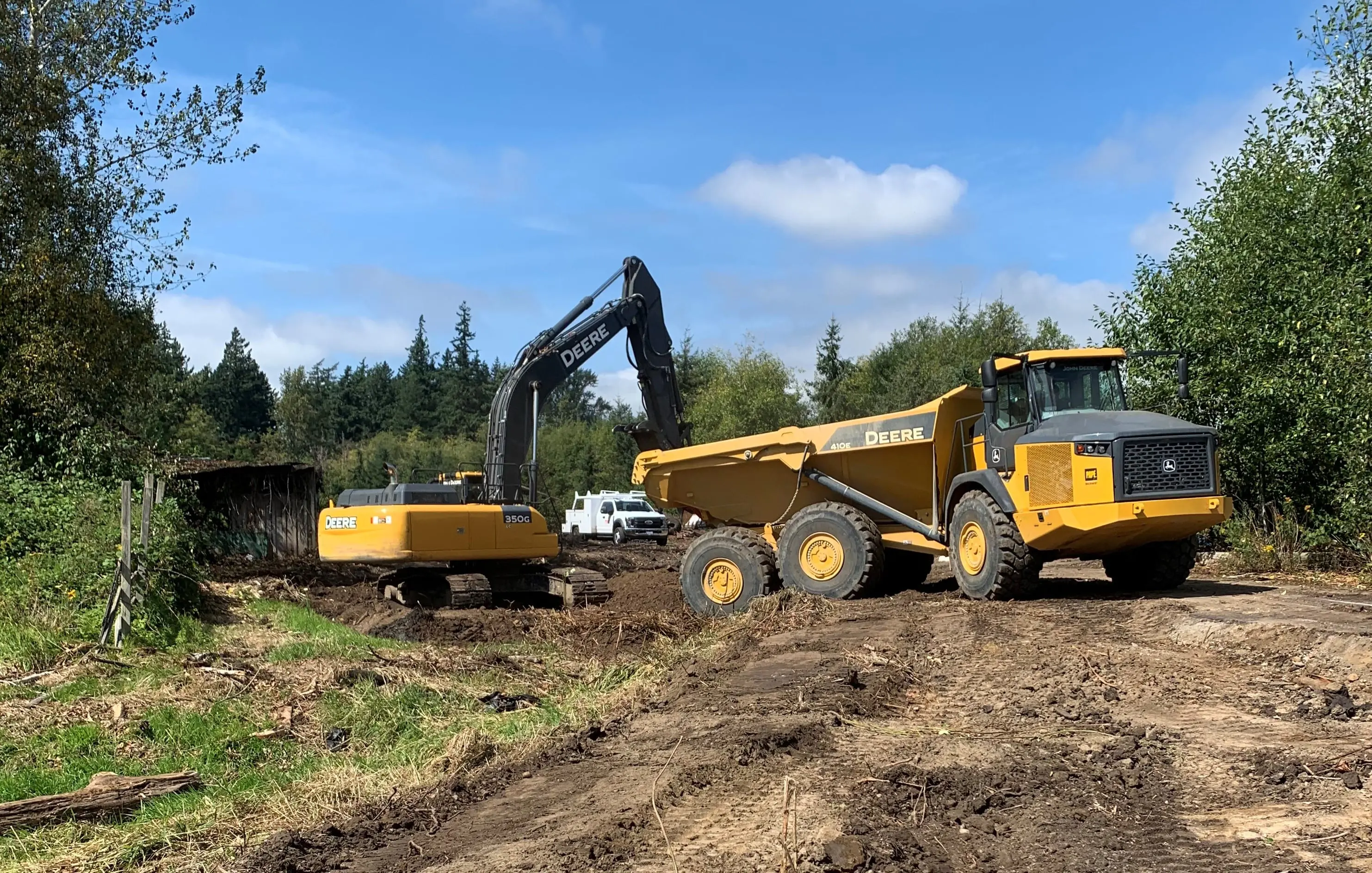 Excavator and dump truck removing debris from natural area