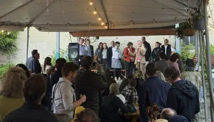 A group of officials speak from a stage to a crowd at an outdoor bar