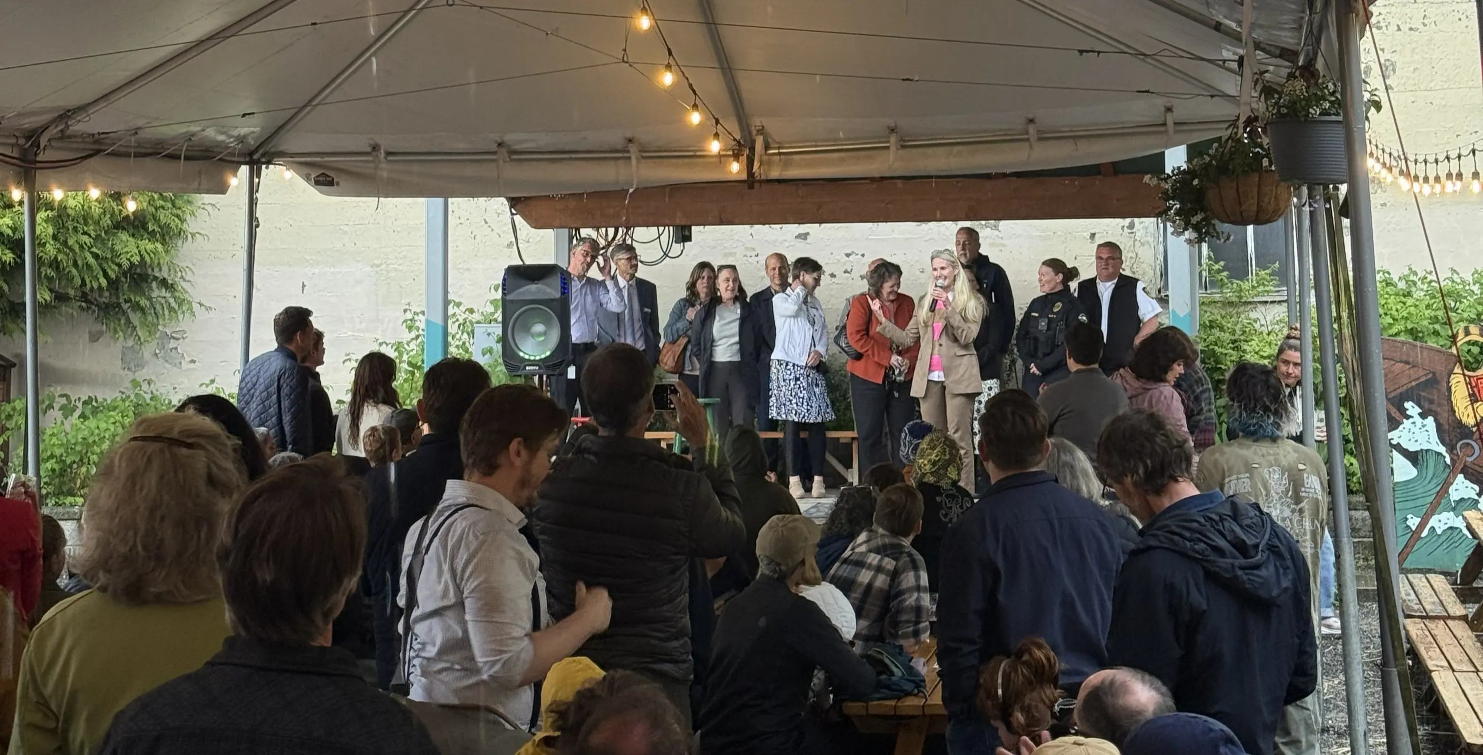 A group of officials speak from a stage to a crowd at an outdoor bar
