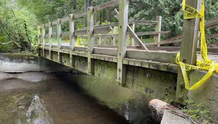 A broken bridge with yellow caution tape over a creek