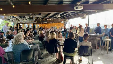 City leaders speak to a large crowd in a brewery.
