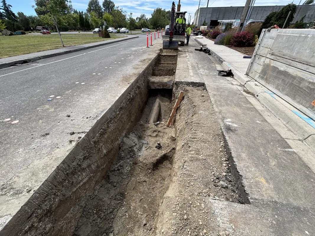 Excavator digging a trench in road for watermain replacement