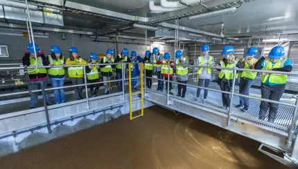 Group of school children in bright yellow vests on a tour looking at a water treatment process.
