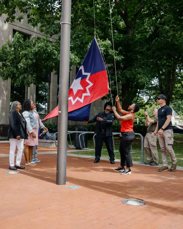 A small group of people raise a Juneteenth flag on a flag pole