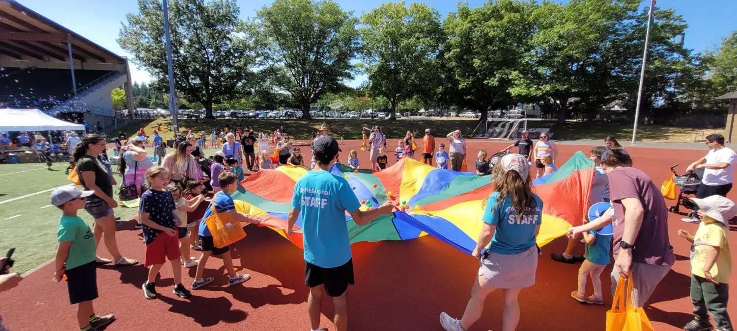 Kids and event staff play with a large parachute