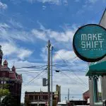 A round building sign reading "Make.Shift Art Space" with a historic building in the background