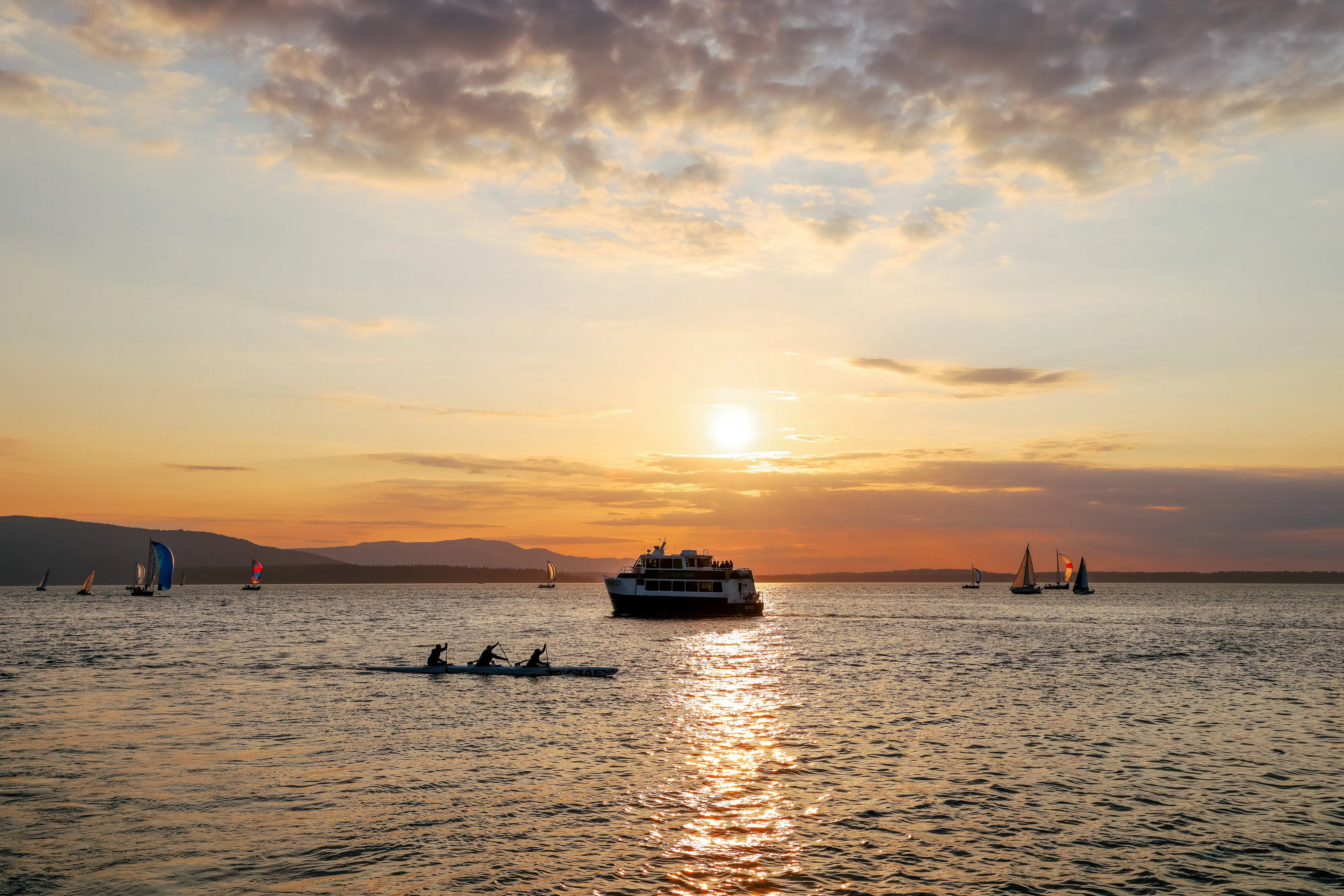 People enjoy Bellingham Bay by ferry, sailboat, and canoe with a sunset in the background