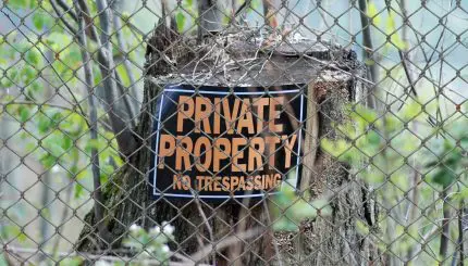 "private property no trespassing" sign on tree stump behind chain link fence