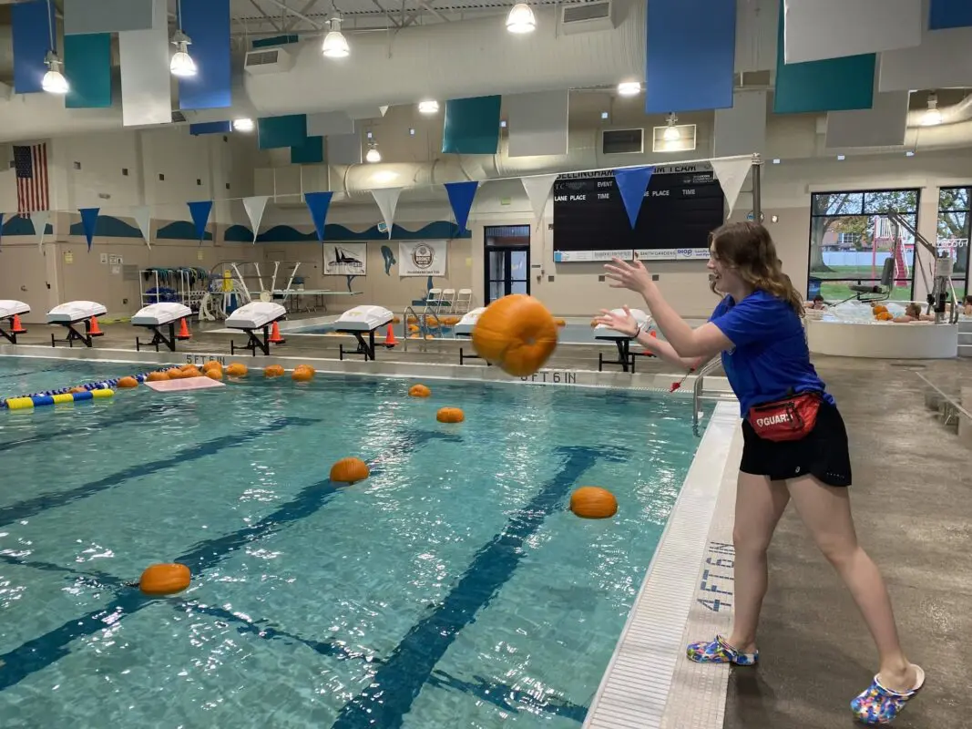 A woman throws a large pumpkin into a pool.