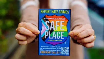 A woman holds up a rainbow sticker that says "Safe Place"