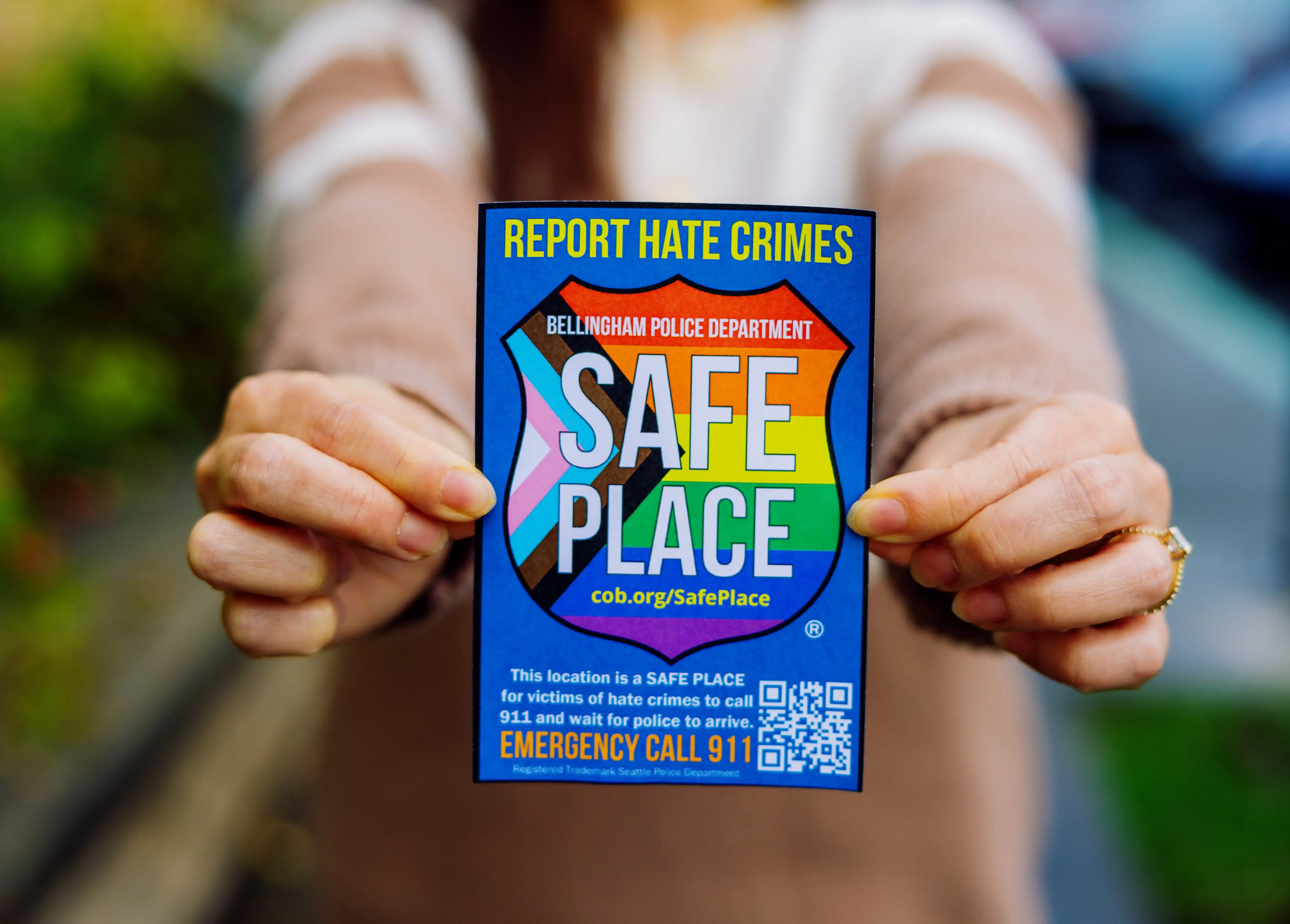 A woman holds up a rainbow sticker that says "Safe Place"
