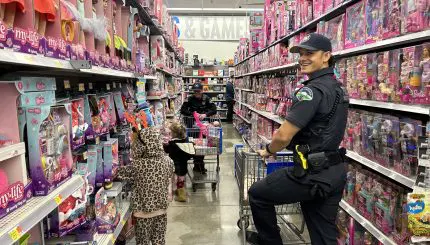 Uniformed officer stands with shopping cart in toy aisle as kids look at toys.