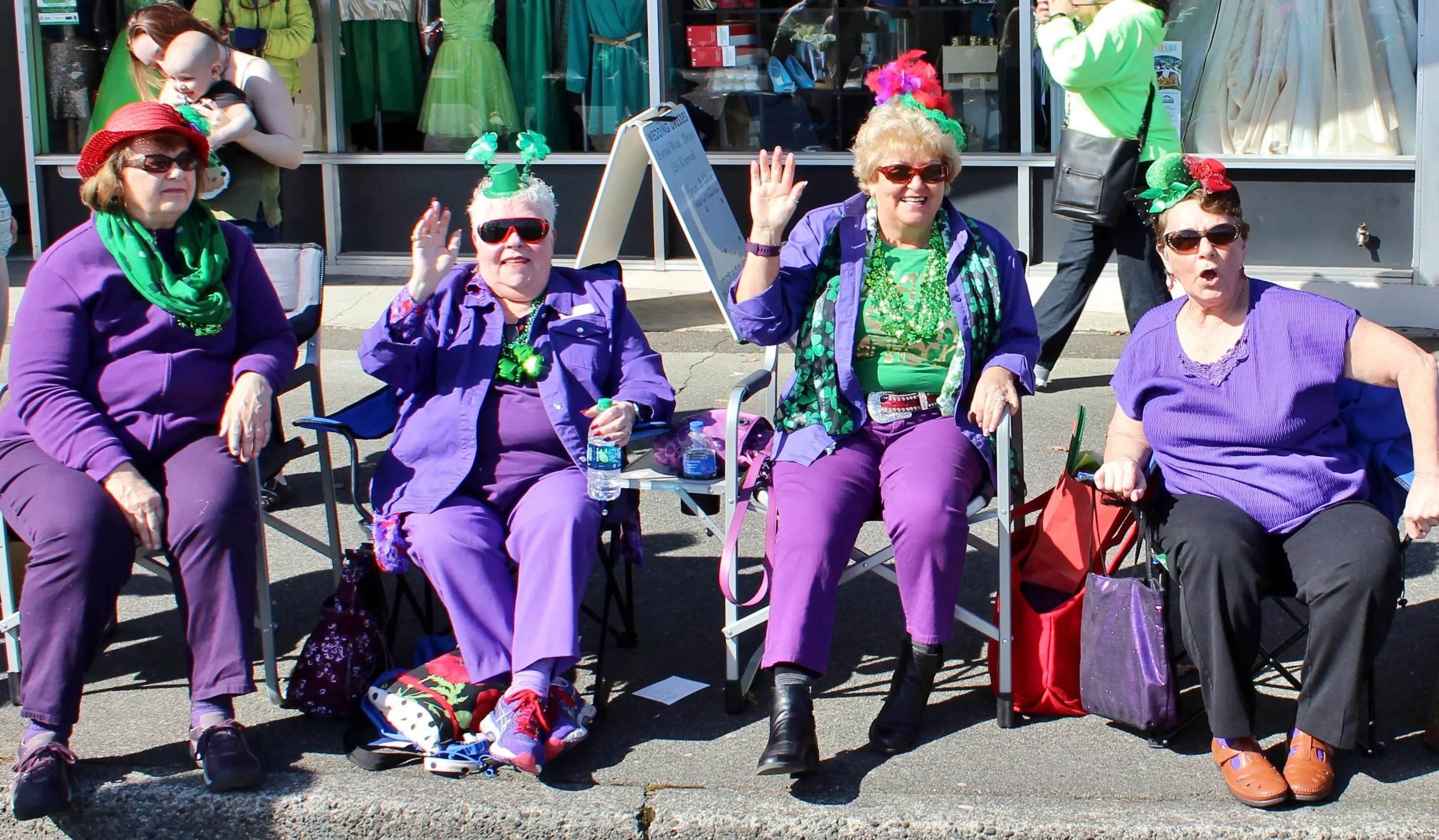 Four women dressed in festive purple and green watch a parade.