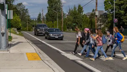 group of youth walking in crosswalk as cars wait