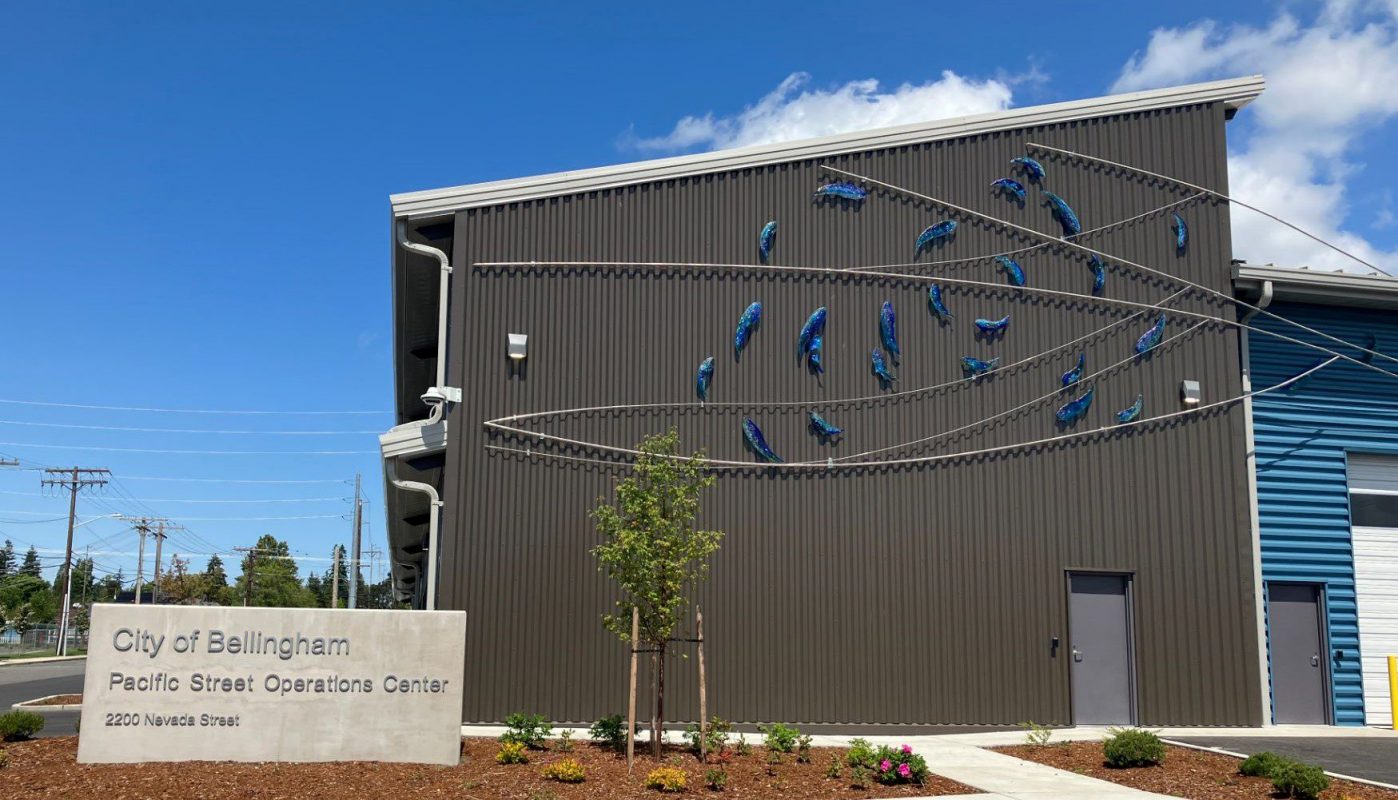 Utility building with 3D art work attached depicting fish swimming in a circle with metal cross sections symbolizing  water currents