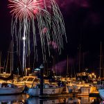 boats docked in harbor at night with bright red firework radiating out and cascading down