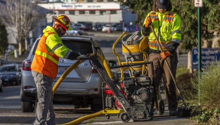 two male public works employees completing sideway repair with large, handheld equipment