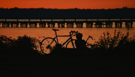 Sunset over the water with a silhouette of two bikes and a person sitting.