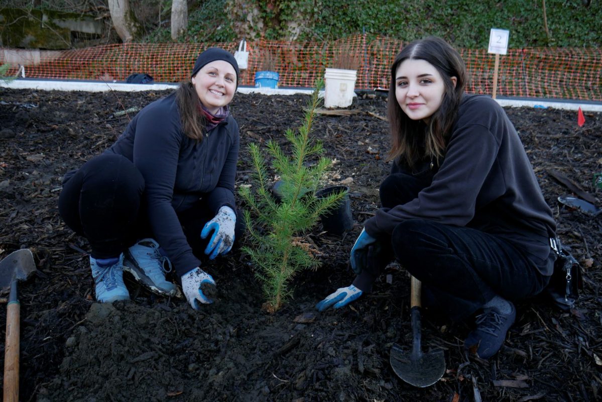 Two people smiling next to a tree they just planted