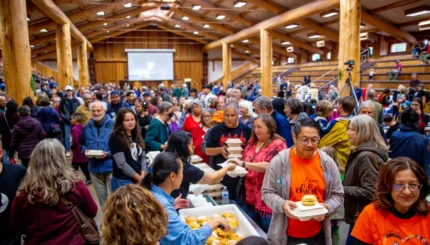 A large group of people pick up containers of food from tables