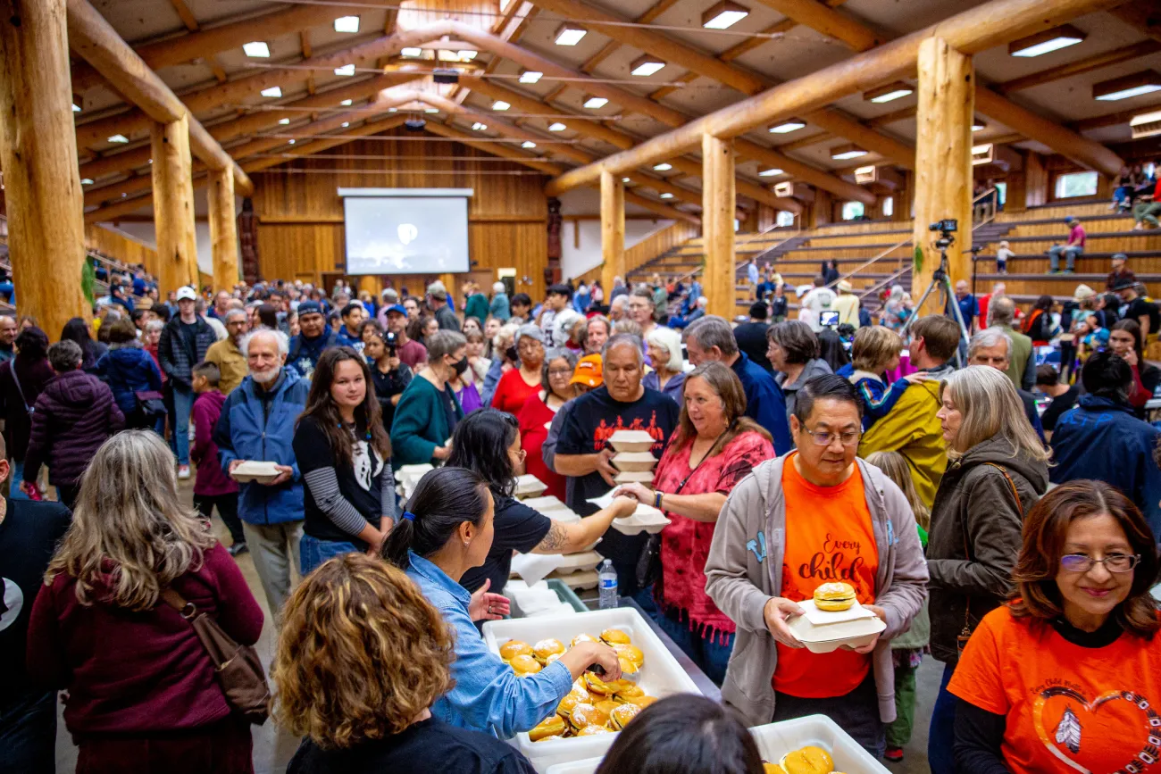 A large group of people pick up containers of food from tables