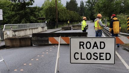 Road closure sign in road with vehicle bridge and construction workers in the background