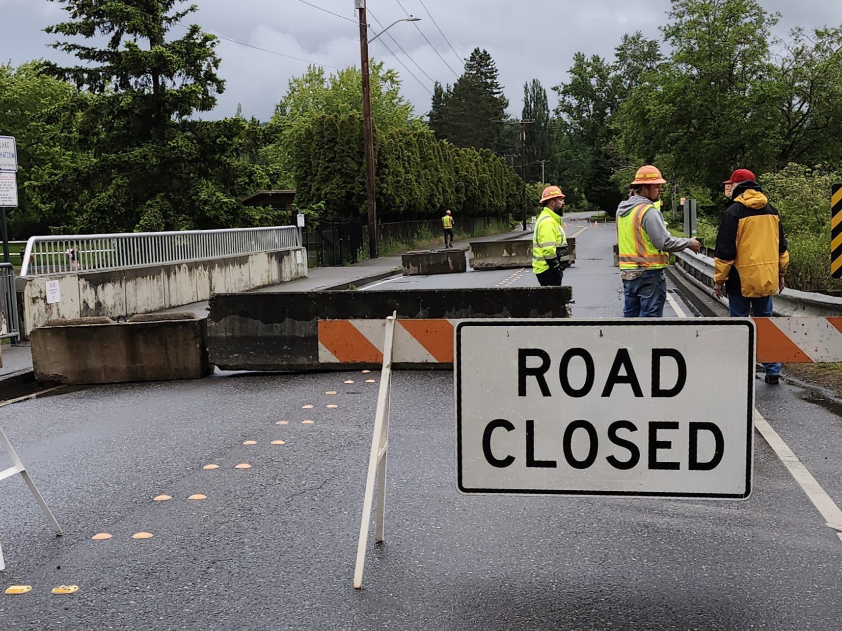 Road closure sign in road with vehicle bridge and construction workers in the background