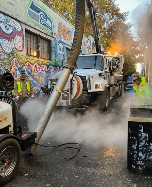 Staff operating a large vactor truck and pressure washer in an alley. 
