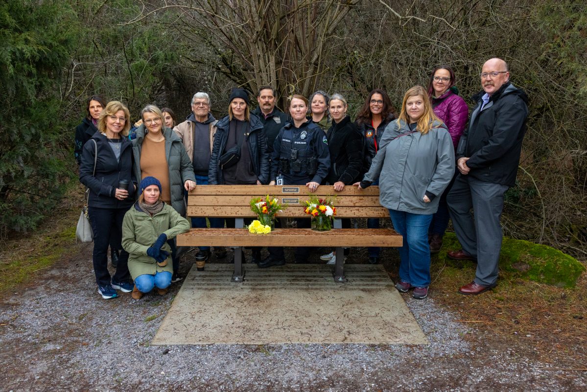 Several people gathered behind a wooden bench with a plaque
