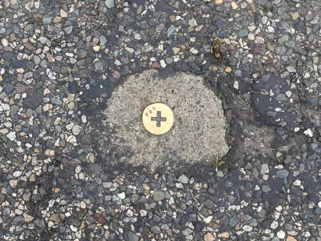Very small metal tack placed in concrete in a street with the number 690 on it.