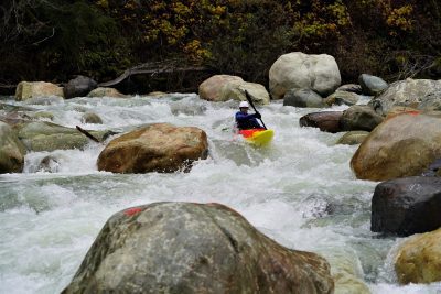 Kayaker in bright yellow and red kayak paddling through rapids in river