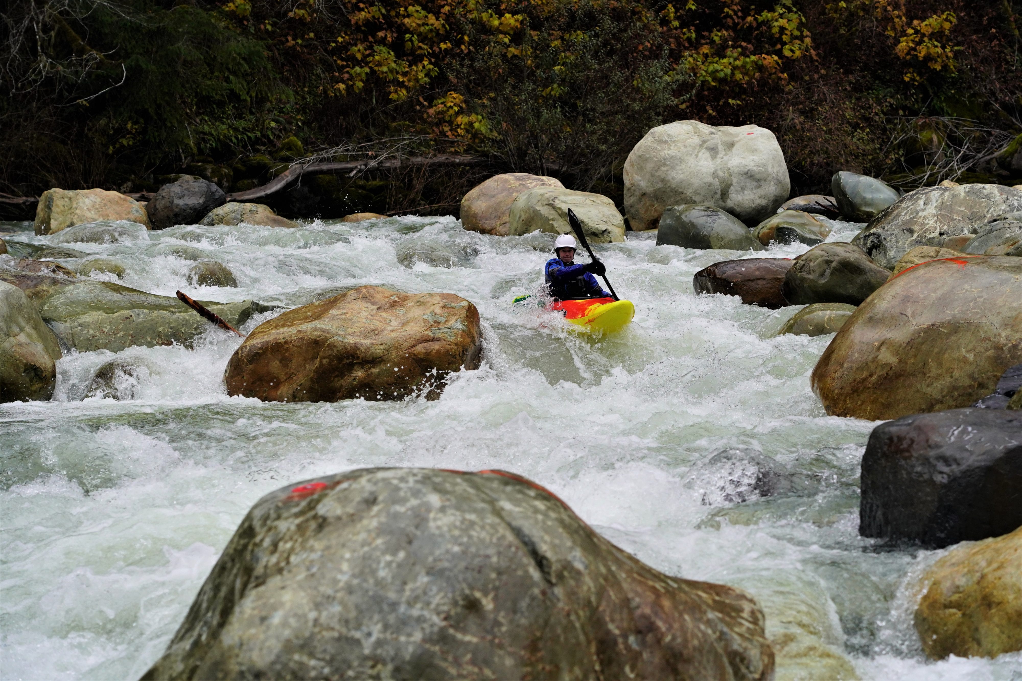 Kayaker in bright yellow and red kayak paddling through rapids in river