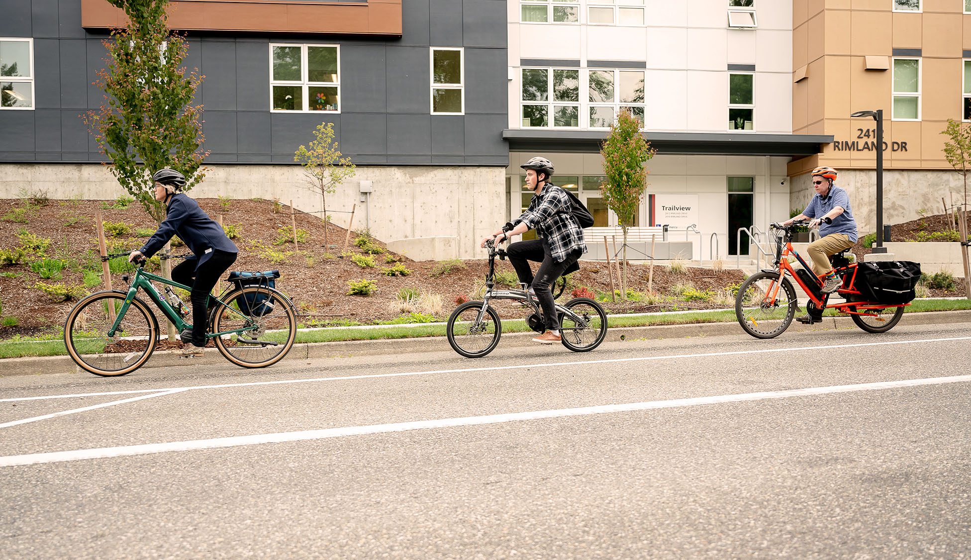 Three people biking in a row in a bike lane on a road in front of a building.