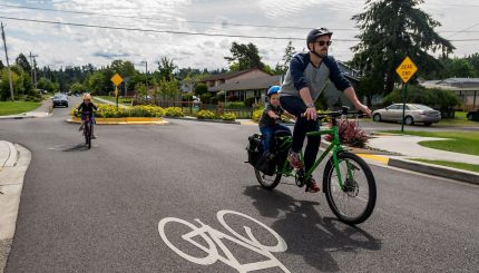 Man and young child riding on bike with older child riding near by