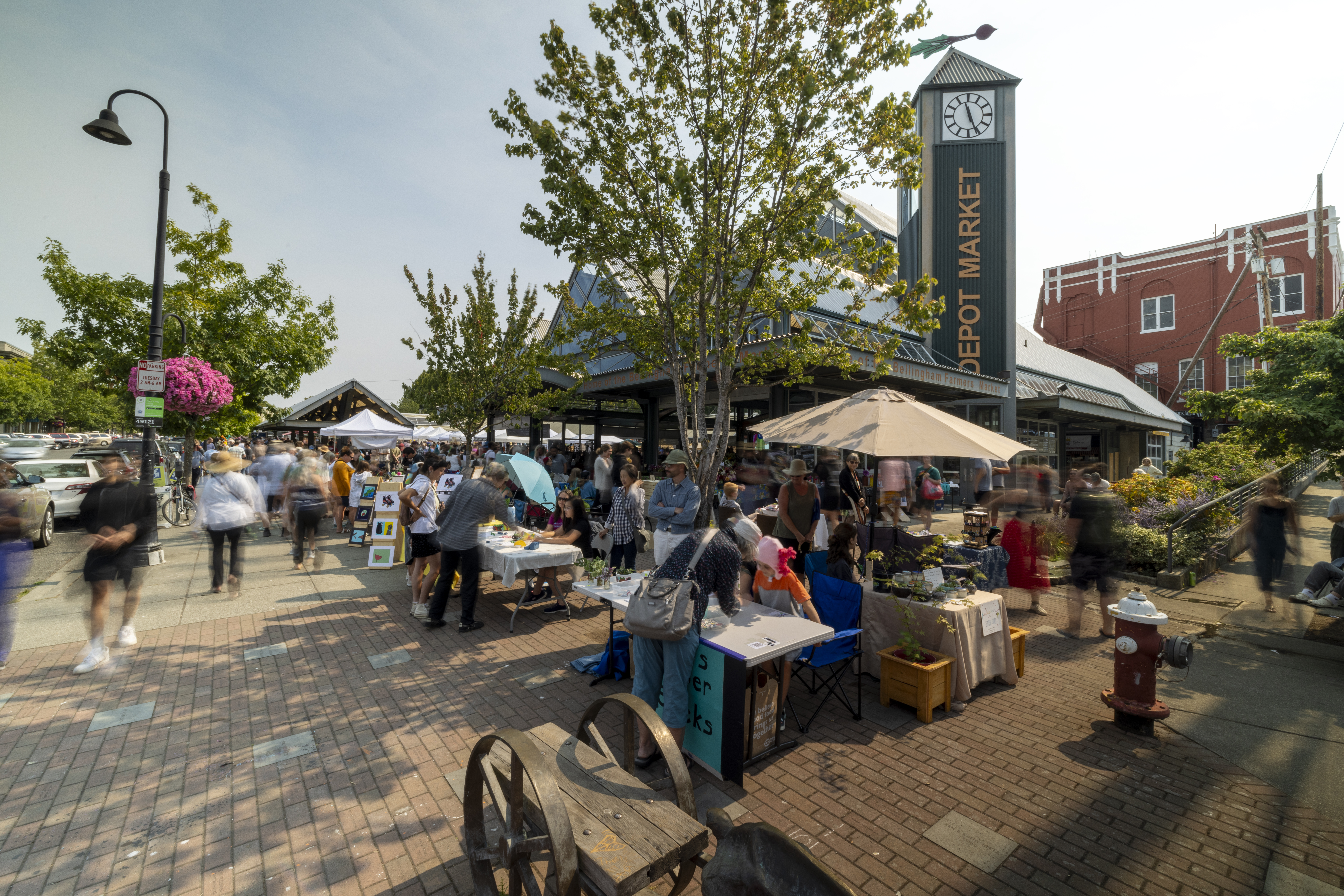 People gather and shop at booths at the Farmer's Market. The Depot Market square building is in the background.