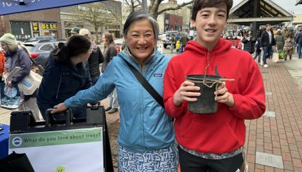 Adult and teenager smiling while holding a small tree at a market