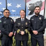 three police officers posing together in full uniforms, smiling