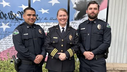 three police officers posing together in full uniforms, smiling