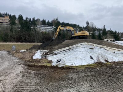 Excavator moving dirt underneath white tarp