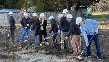People wearing hard hats pose with shovels in an empty lot.