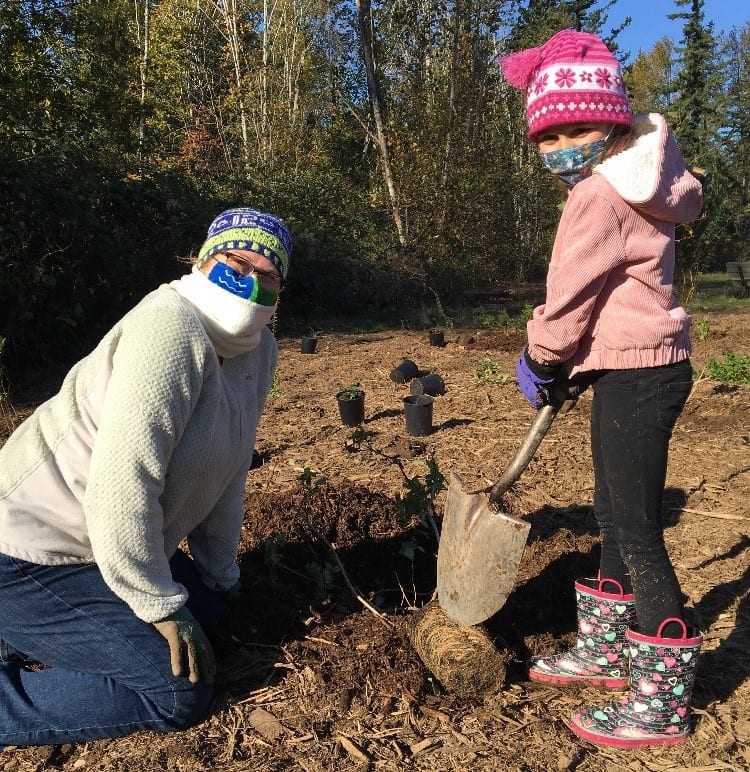 Woman and young girl wearing masks and digging a hole 